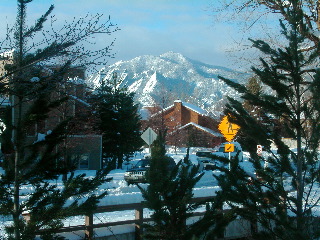 Cars pinned in by snow banks, trees looking a little ragged, morning sunshine on the snow-covered Flatirons